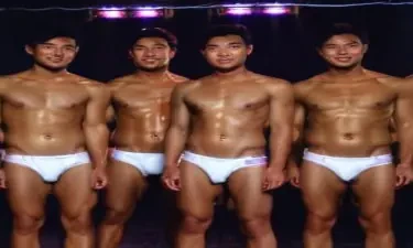 Ten smooth lean Asian male models with different faces are standing still on a stage in front of an audience in a dark room. Neon lights. They are all only wearing white thongs underwear. Zoom slowly to show smiling faces.